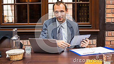 Hard working smiling businessman in restaurant with laptop and pad.
