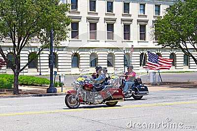 Harley Davidson colorful motorcycles travel on Independence Avenue under American flag.