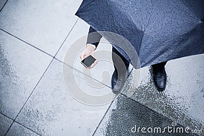 High angle view of businessman holding an umbrella and looking at his phone in the rain