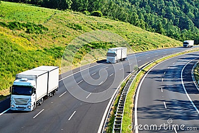 Highway with three oncoming white truck in a woode
