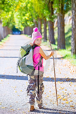 Hiking kid girl with walking stick and backpack in autumn