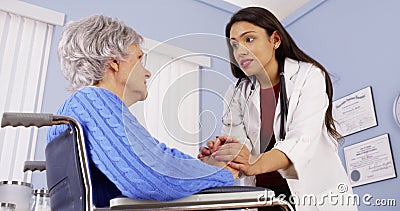 Hispanic woman doctor comforting disabled elderly patient