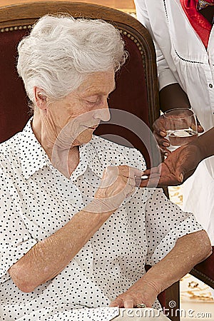 Home nurse giving elderly woman vitamin pills at home