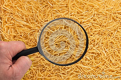 Human hand holding a magnifying glass over the pasta