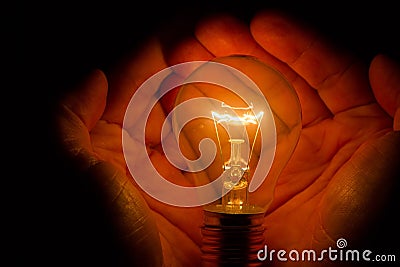 Human hands holding a light bulb to conserve energy darkness