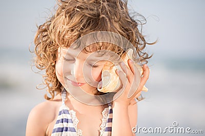 Il bambino felice ascolta la conchiglia alla spiaggia