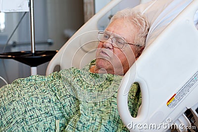 Un uomo anziano white-haired si siede in su in un letto di ospedale e sembra felice. Porta un abito verde dell&#39;ospedale, porta i vetri ed è di peso ... - il-paziente-ricoverato-maschio-anziano-sta-visualizzando-25649464