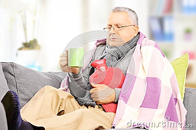 Ill man on a sofa covered with blanket drinking hot tea at home
