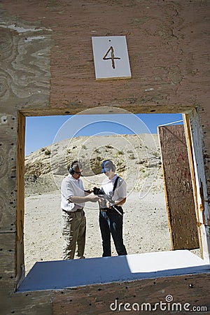 Instructor Assisting Woman At Firing Range In Desert