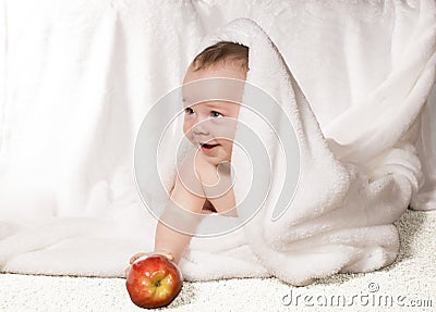Joyful baby with red apple under a white blanket