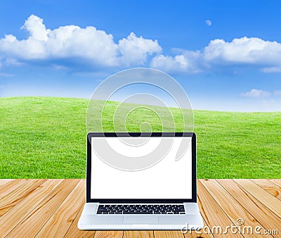 Laptop computer on wooden floor with green fields and blue sky b