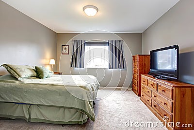 Large grey bedroom with dresser, tv and blue curtains.