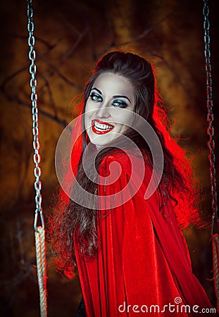 Laughing halloween woman in red cloak on the swing