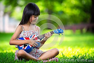 Little asian girl sitting on grass and play ukulele