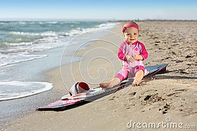 Little baby girl on the sand beach with surf board
