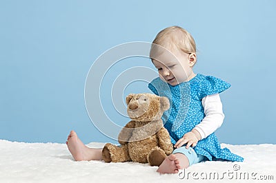 Little baby girl with teddy bear, on blue