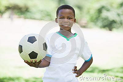 Little boy holding football in the park smiling at camera