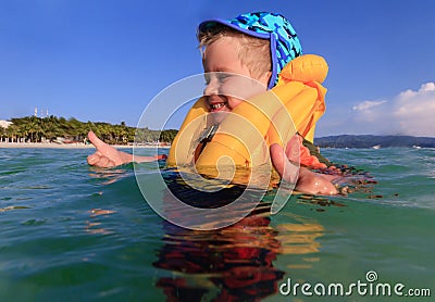 Little boy in life jacket playing with water on the beach
