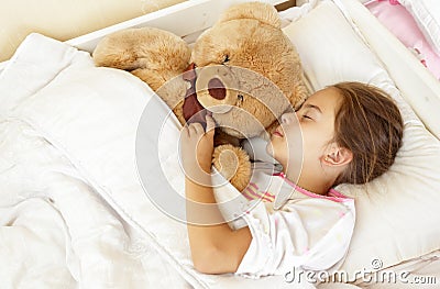 Little brunette girl sleeping in bed with teddy bear