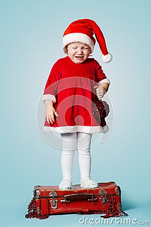 Little crying girl standing on red suitcase