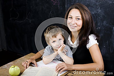 Little cute boy with teacher in classroom, siting at table with books