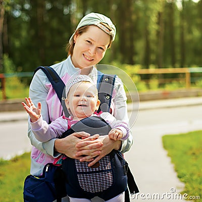 Little cute girl in sling. Mother`s hand hold her. Summer time