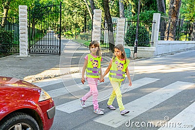 Little elementary school kids crossing the street wearing a vest with the stop sine on it.