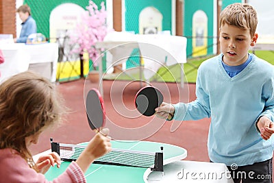 Little girl and boy in blue play table tennis in park