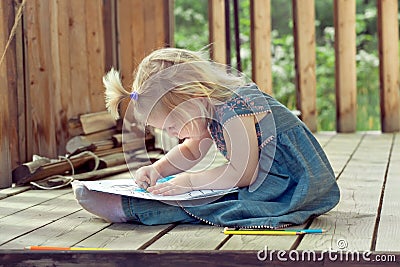 Little girl drawing with colored pencils on a country house wood