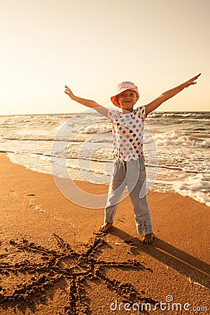 Little girl draws sun on sand at the beach