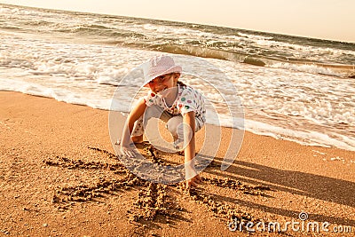 Little girl draws sun on sand at the beach