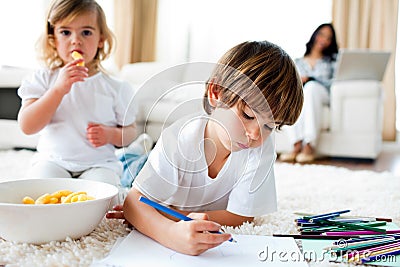Little girl eating chips and her brother drawing