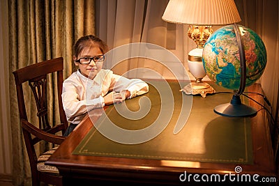 Little girl in eyeglasses sitting behind desk