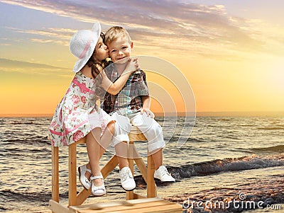 Little girl kissing boy on sea landscape at sunset