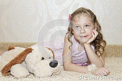 Little girl lying on the carpet with a plush dog