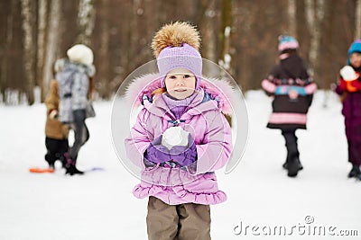 Little girl in pink jacket with fur collar stands in winter park