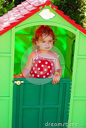 Little girl playing in toy house in the garden