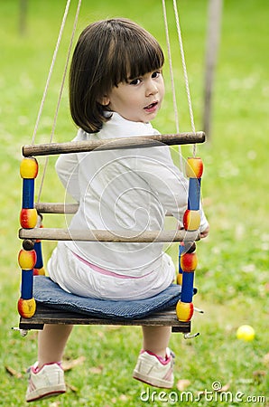Little girl riding on a swing on a green backgroun