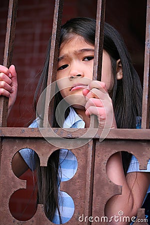 Little girl standing behind iron bars