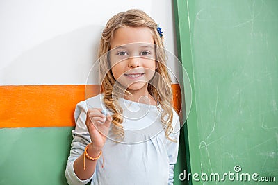 Little Girl Standing By Green Chalkboard In