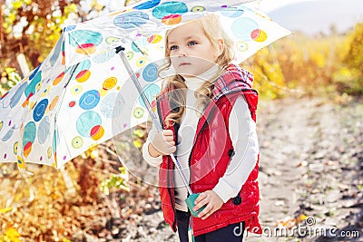 Little girl with umbrella in red vest outdoor