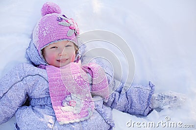 Little smiling girl in scarf and hat lies on snow at winter