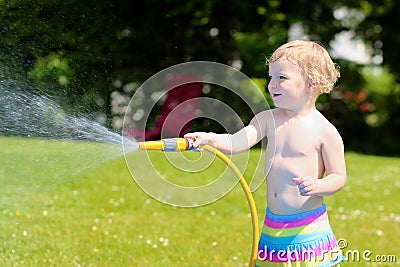 Little toddler girl playing with water hose in the garden