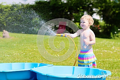 Little toddler girl playing with water hose in the garden