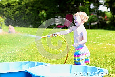 Little toddler girl playing with water hose in the garden