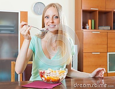 Long-haired blonde girl eating fruit salad in home