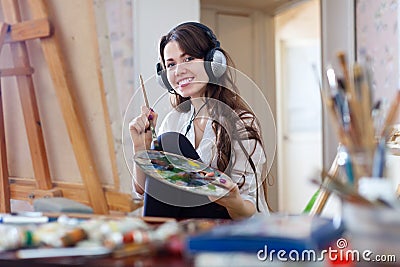 Long-haired woman in headphones paints with oil colors