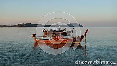 Long tail boat anchored in the sea by the dawn with the blue sky and the island in the background
