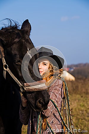 Lovely blond woman in a hat standing by horse