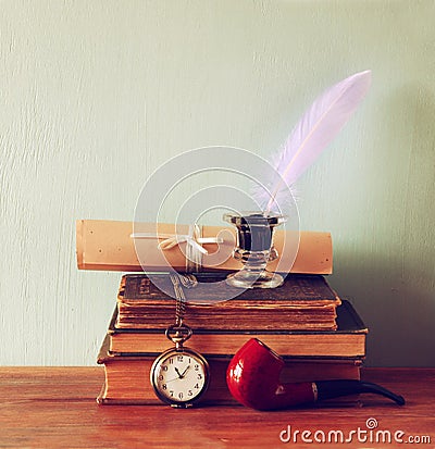 Low key image of white Feather, inkwell, scroll ancient books on old wooden table